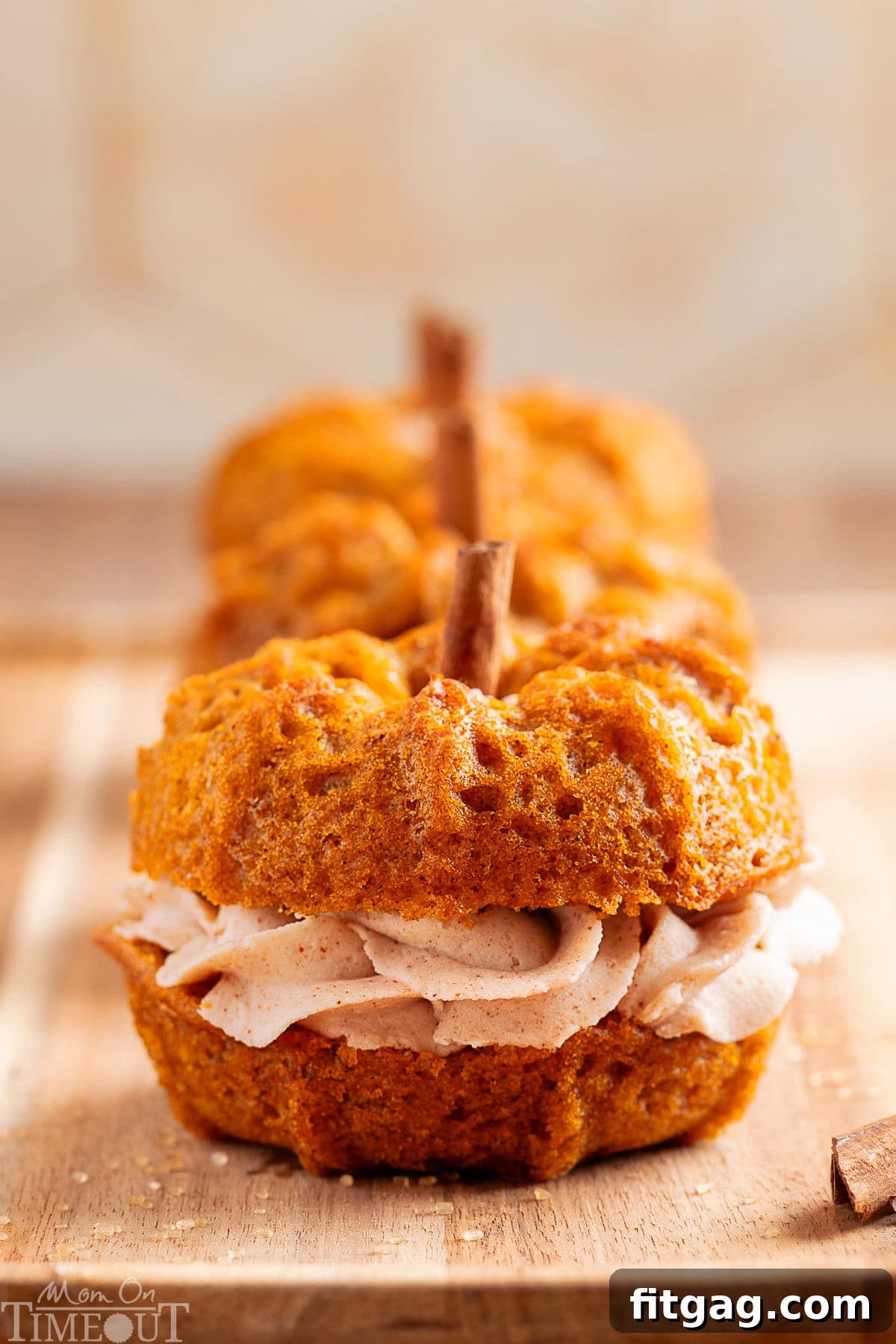 Three mini pumpkin bundt cakes lined up in a row on a wood board. Each cake is sandwiched together with brown butter frosting.