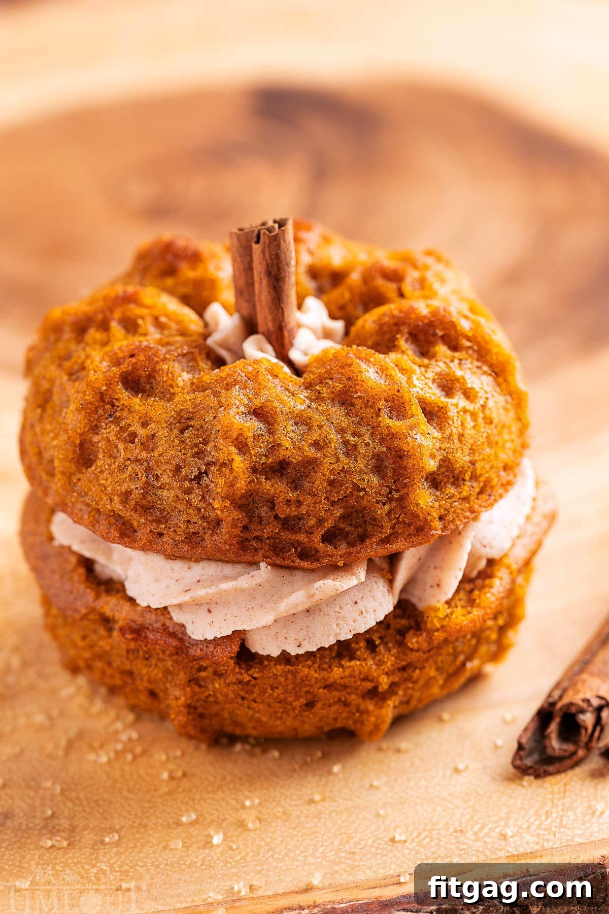 Mini pumpkin bundt cake made with two small bundts and sandwiched with cinnamon brown butter frosting. The stem is a cinnamon stick. The cake is sitting on a wood board.