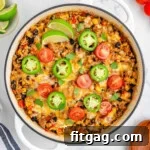 Top down view of taco rice in a white skillet topped with jalapeno slices, lime wedges and tomatoes. More taco topping can be seen scattered around the edge of the skillet.