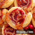 Top down shot of brie and cranberry puff pastry pinwheels stacked on a wood board.