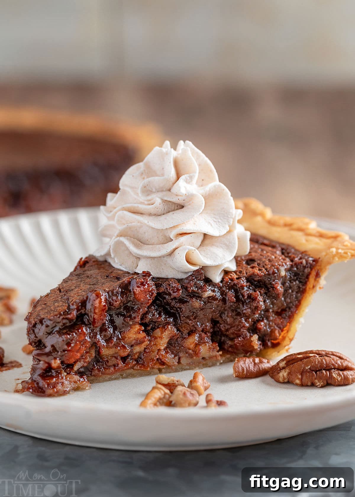A generous slice of Chocolate Bourbon Pecan Pie on a pristine white plate, elegantly topped with fluffy bourbon cinnamon whipped cream. The full pie rests invitingly in the background, promising more deliciousness.
