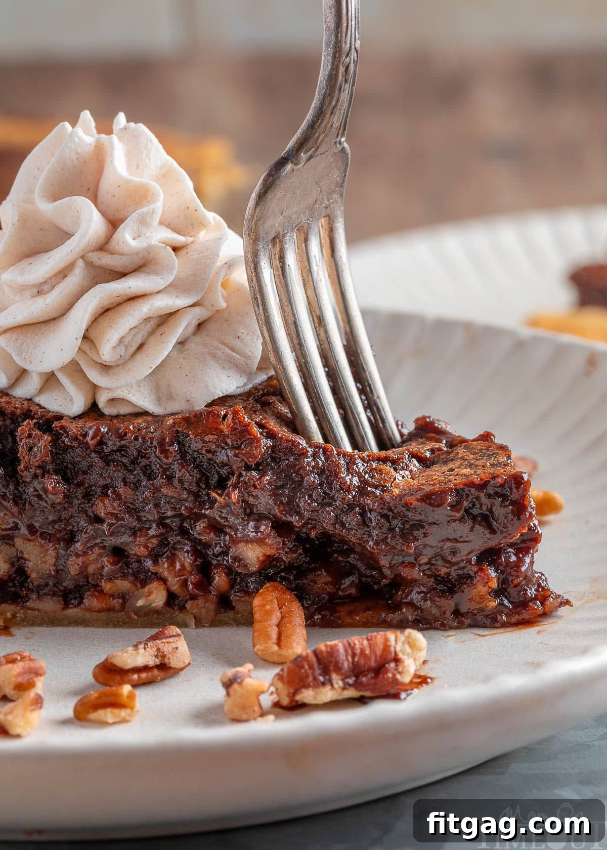 A fork elegantly cuts into the side of a slice of bourbon chocolate pecan pie, resting on a white plate, highlighting its rich layers and tempting texture.