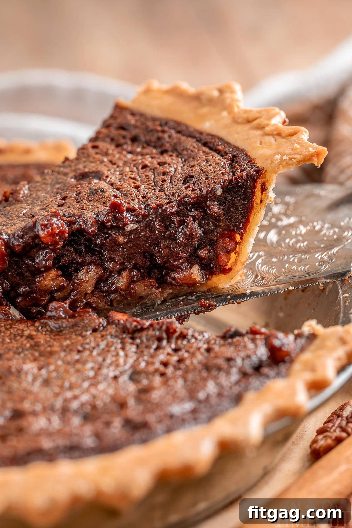 A perfect slice of chocolate pecan pie with bourbon is gently lifted out of the pie plate, showcasing its golden crust and rich, dark filling.