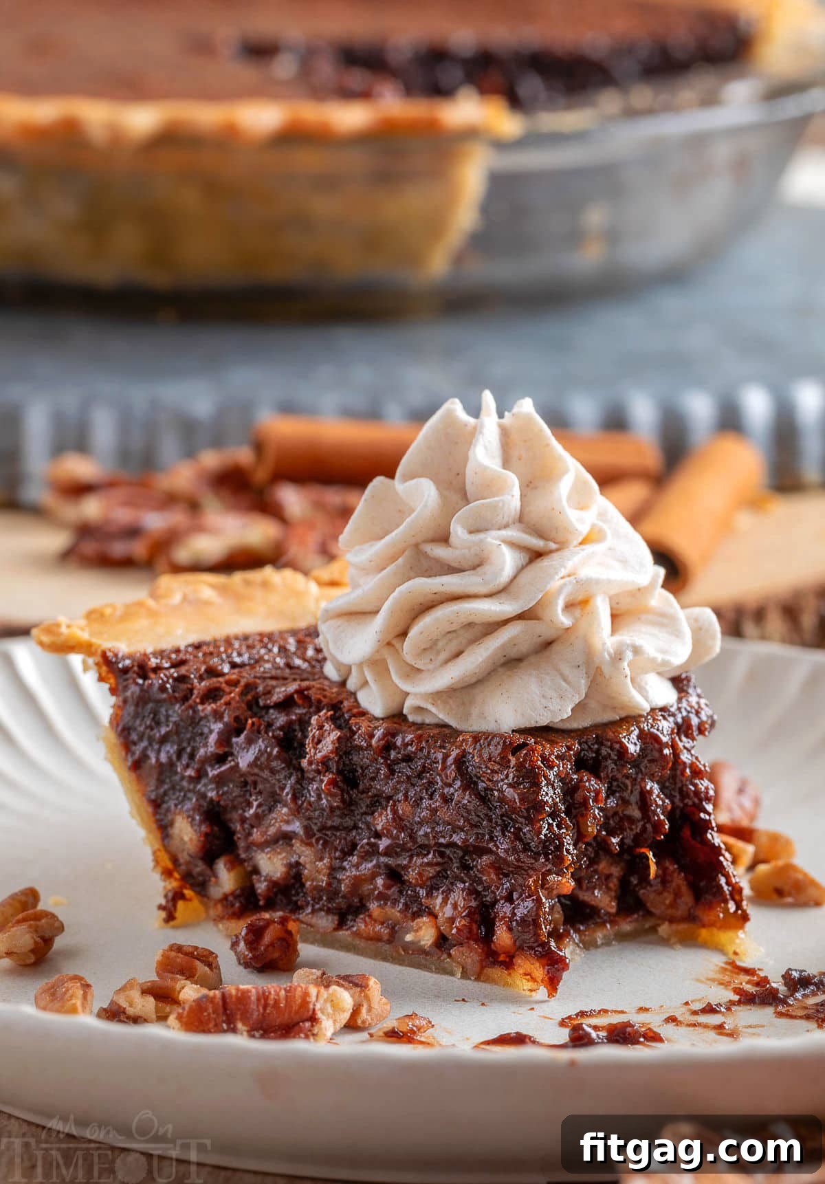 A generous slice of Chocolate Bourbon Pecan Pie on a white plate, topped with creamy whipped cream. A bite has been taken, revealing the rich, gooey interior. The whole pie is subtly visible in the background.
