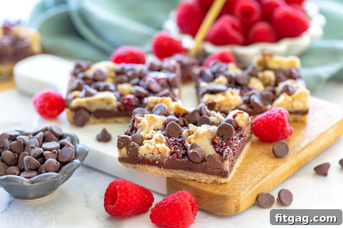 Decadent Raspberry Crumble Squares 3 Wide shot of three bars sitting on a small white marble and wood cutting board next to each other with chocolate chips and raspberries sprinkled around them.