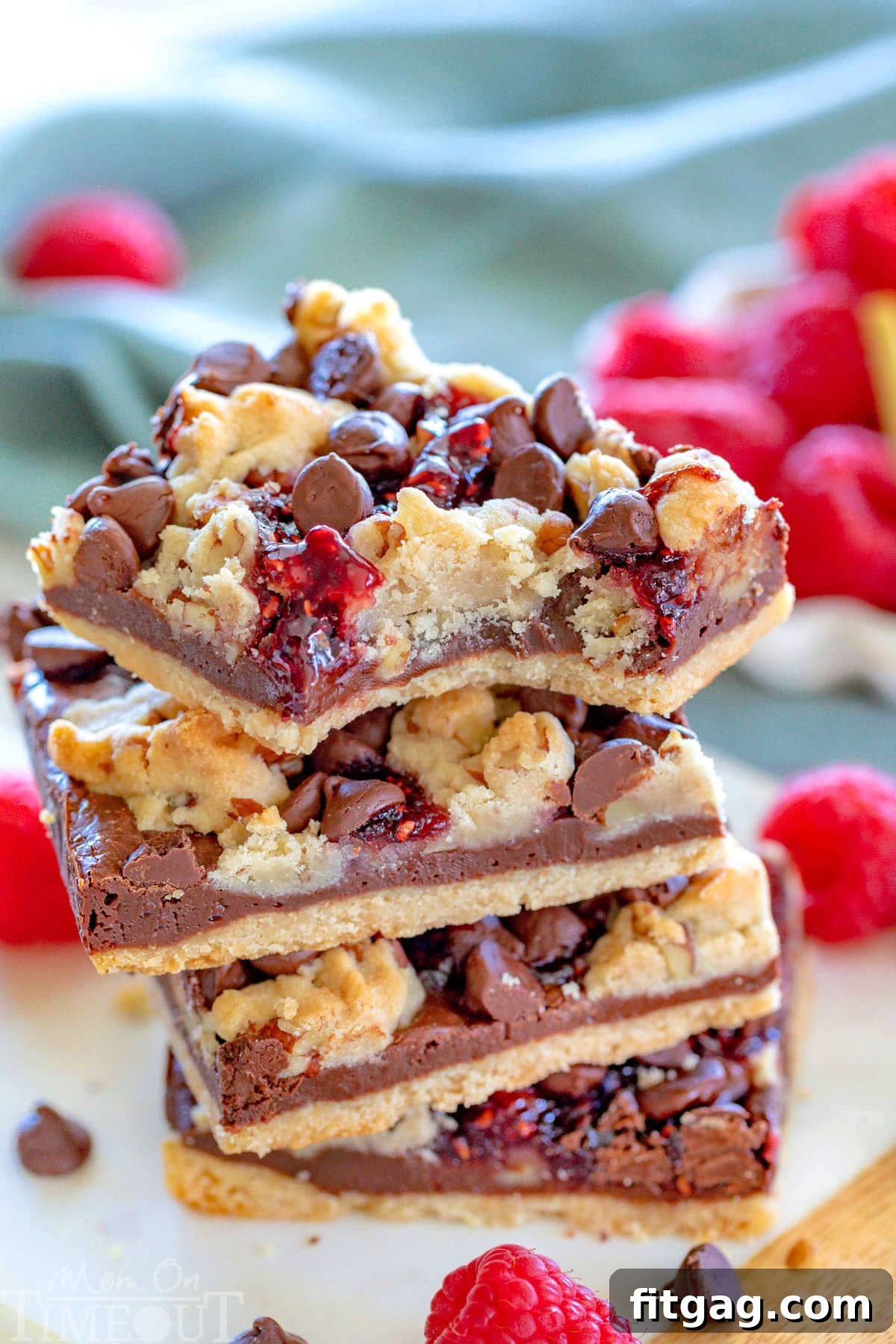 Decadent Raspberry Crumble Squares 8 Four raspberry chocolate crumble bars stacked on small marble board with fresh raspberries in background.
