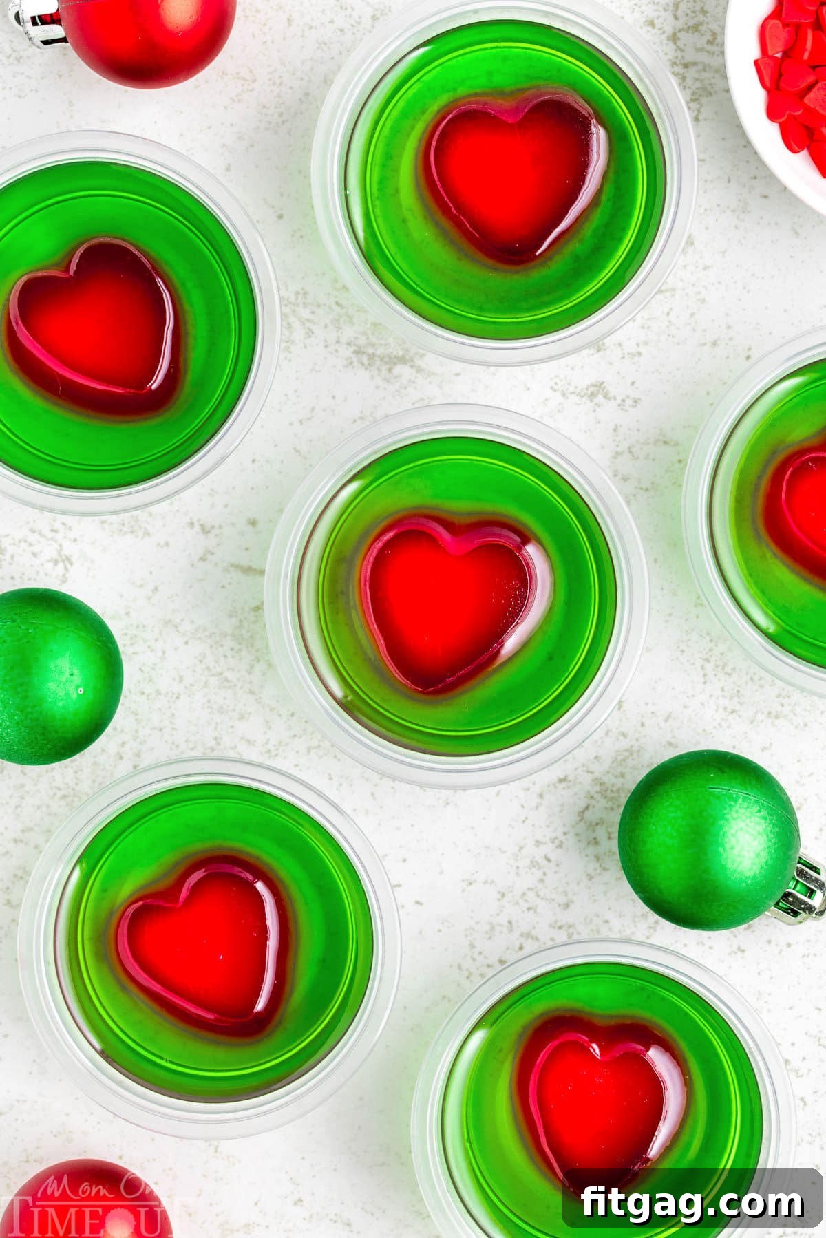 A top down view of a bunch of Grinch Shots on a white surface, garnished with red hearts.