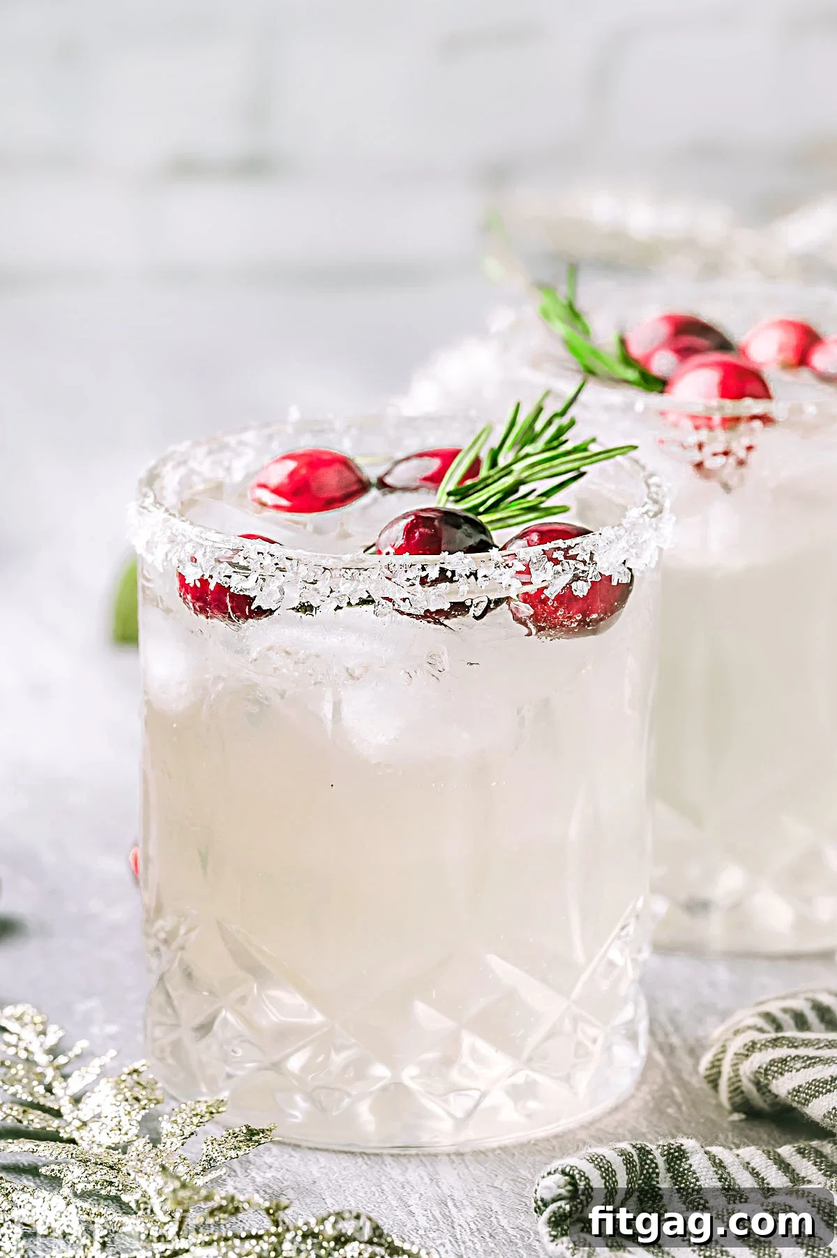 Two exquisite White Christmas Margaritas presented on a crisp white surface, each flawlessly garnished with bright cranberries and fragrant rosemary, ready to be enjoyed.