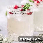 Christmas margarita in a short glass topped with fresh cranberries and a sprig of rosemary, Another glass can be seen in the background.
