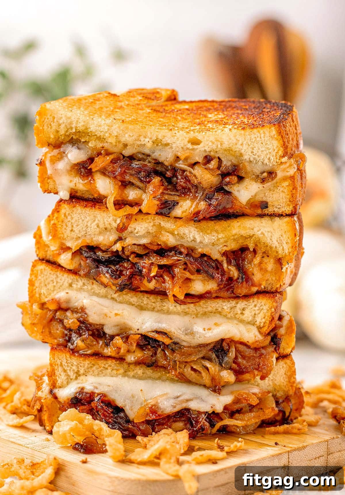 A towering stack of French Onion Grilled Cheese halves on a rustic wooden cutting board, showcasing perfectly golden-brown bread, glistening caramelized onions, and luscious melted cheese oozing from between the layers.