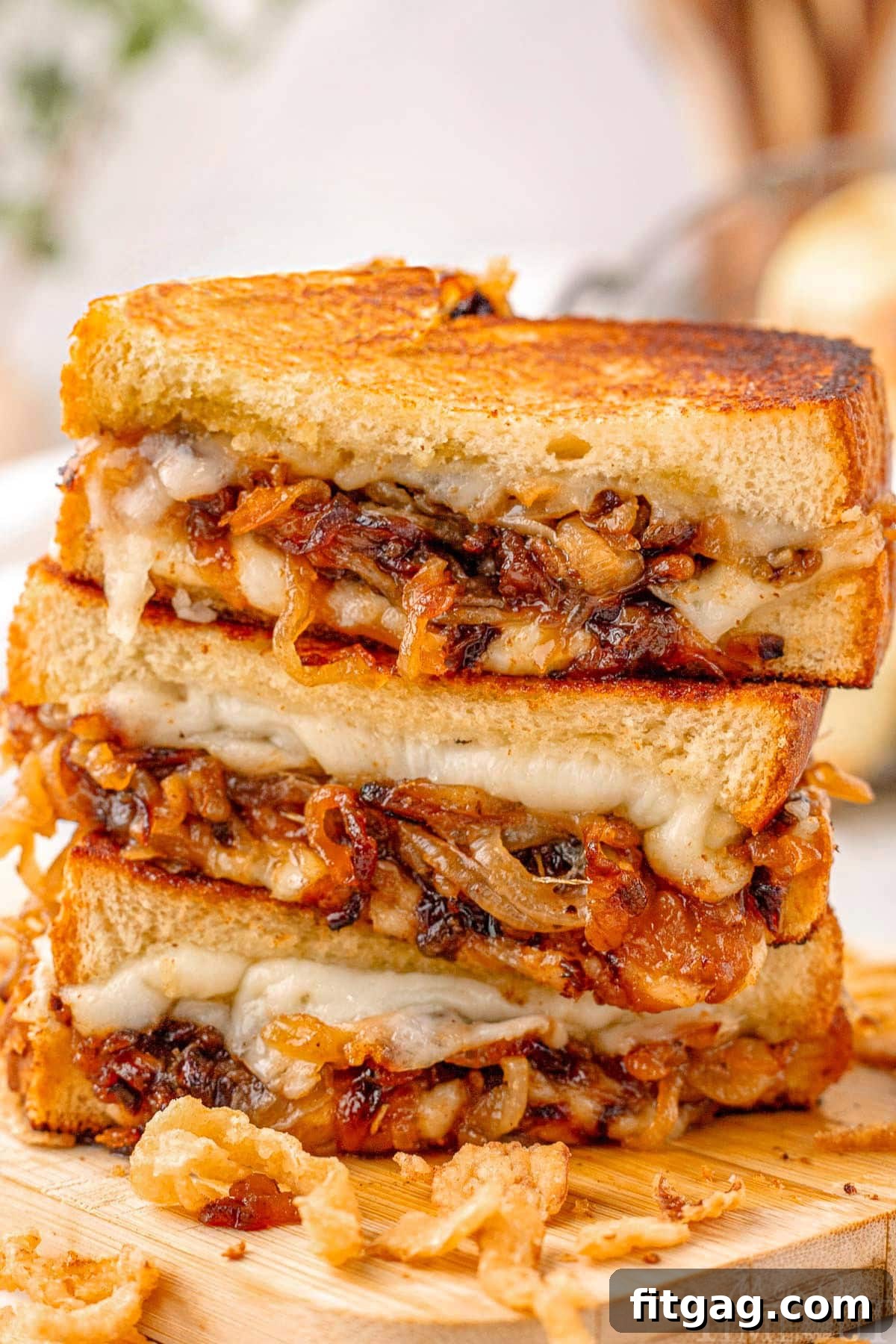 Three halves of a French Onion Grilled Cheese sandwich, artfully arranged and stacked on a wooden cutting board, with a sprinkle of crispy fried onions as a delightful garnish.