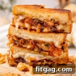 A shot of three halves of a french onion grilled cheese sandwich stacked on a wood cutting board with french fried onions surrounding it.