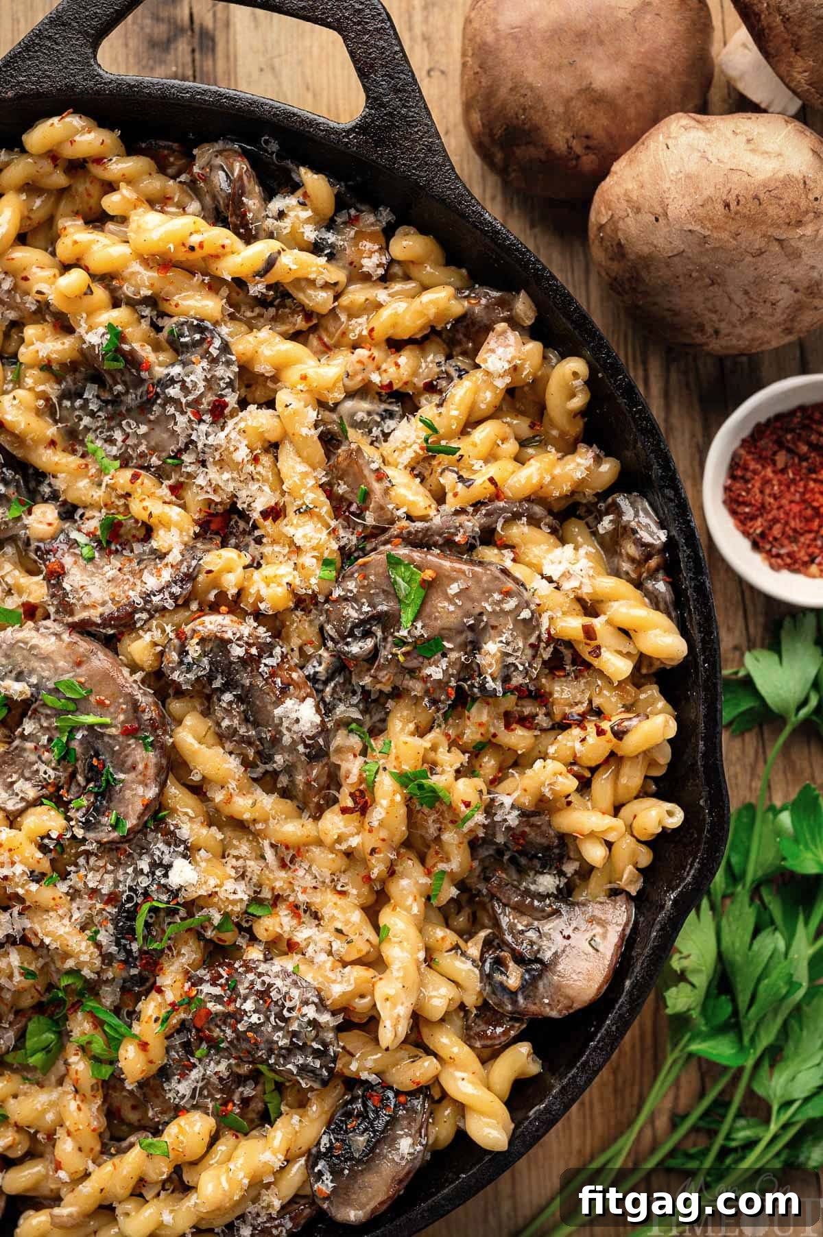 Close-up look at a rich mushroom pasta sauce simmering in a cast iron skillet, beautifully arranged next to fresh mushrooms and herbs on a wooden surface, highlighting the fresh ingredients and depth of flavor.