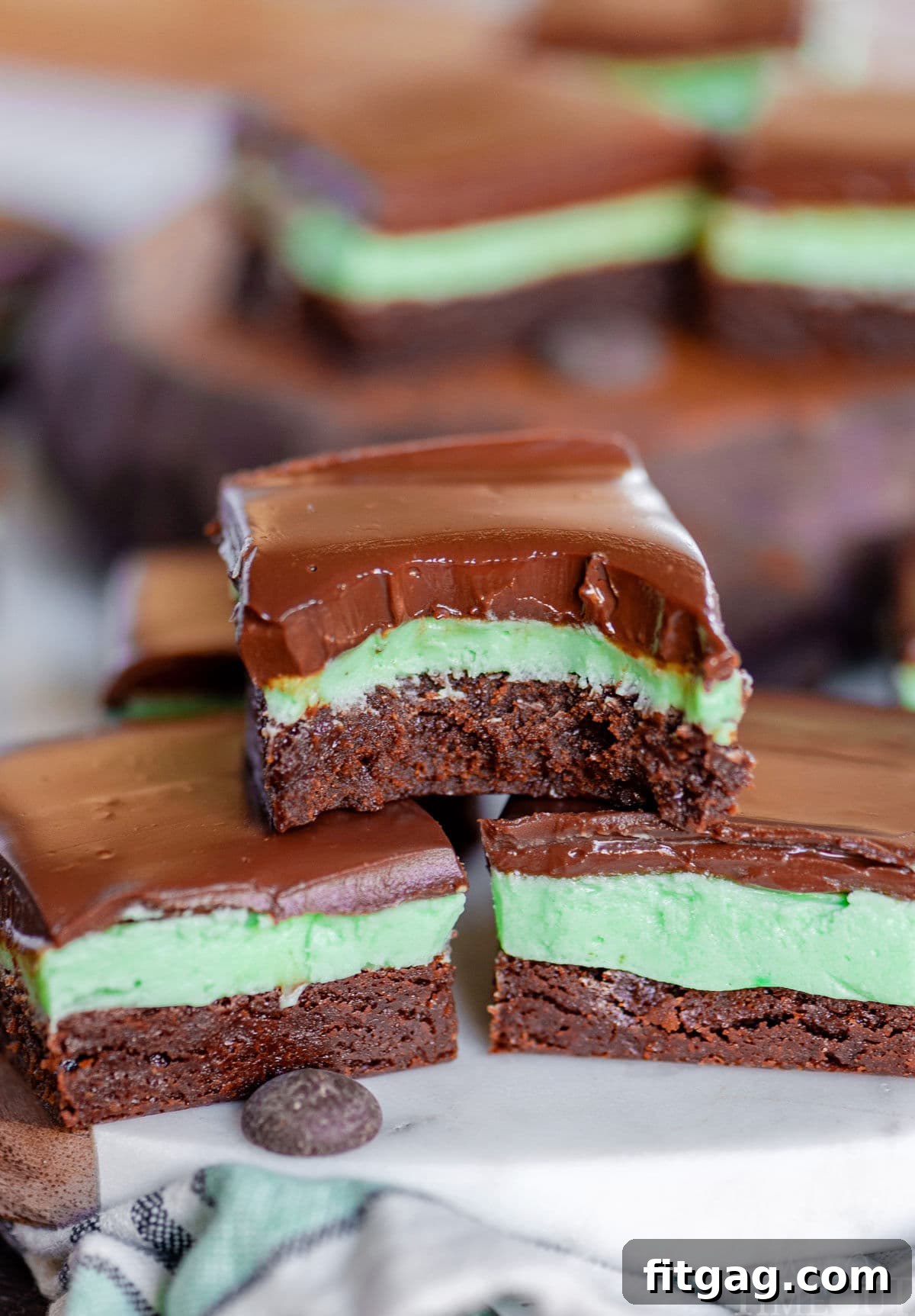 Refreshing Mint Chocolate Brownies 2 Three decadent mint brownies stacked in a pyramid, with a bite taken out of the top one to reveal the layers. More brownies are visible in the background.
