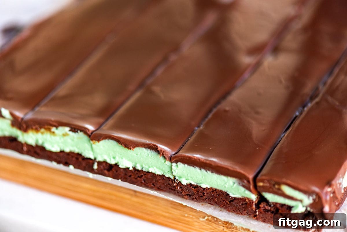 Refreshing Mint Chocolate Brownies 3 A wide shot of freshly cut chocolate mint brownies on a cutting board, clearly showing the three distinct layers: brownie, mint filling, and chocolate ganache.