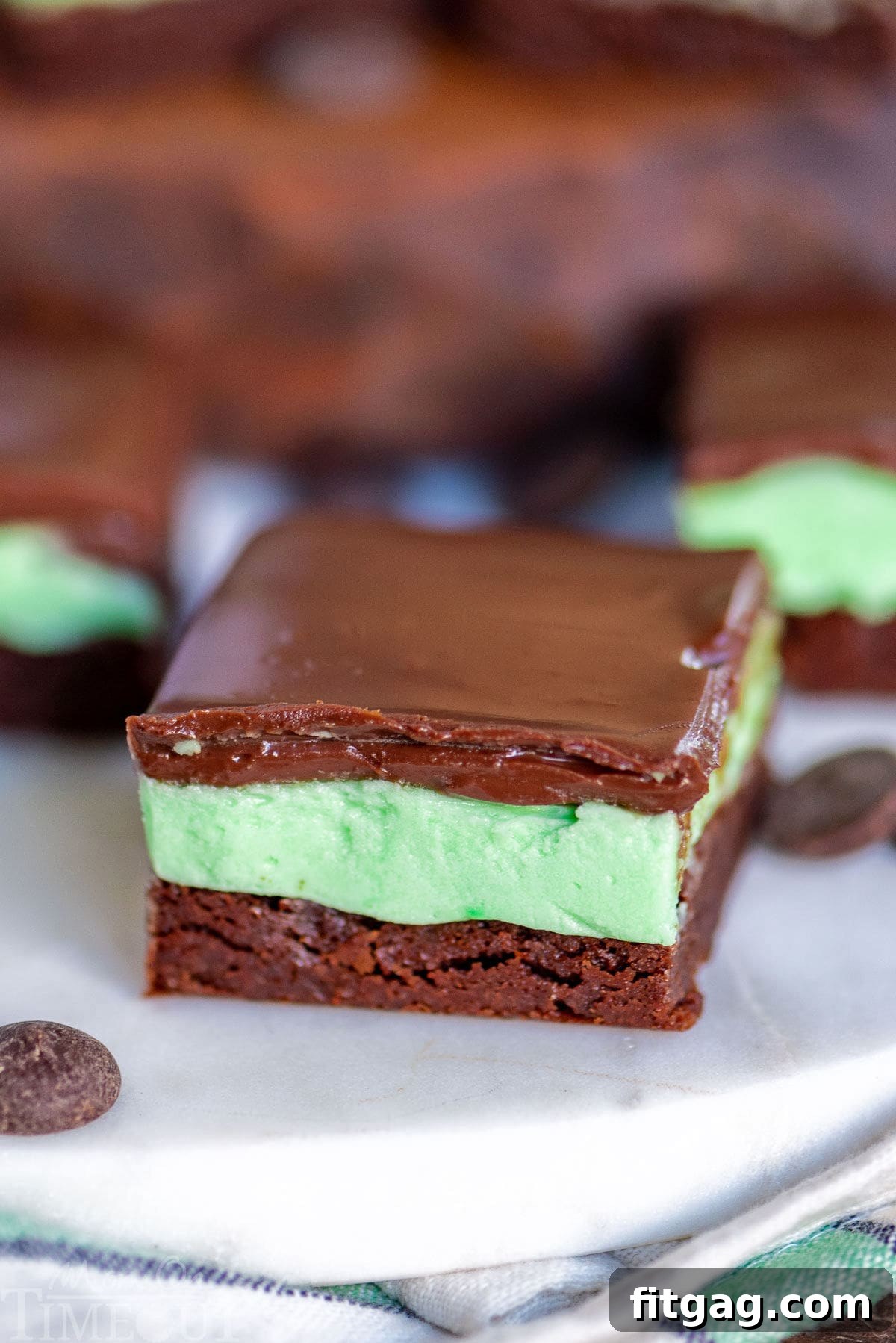 Refreshing Mint Chocolate Brownies 5 A single, perfectly sliced chocolate mint brownie rests on a marble surface, showcasing its irresistible layers, with more brownies softly blurred in the background.