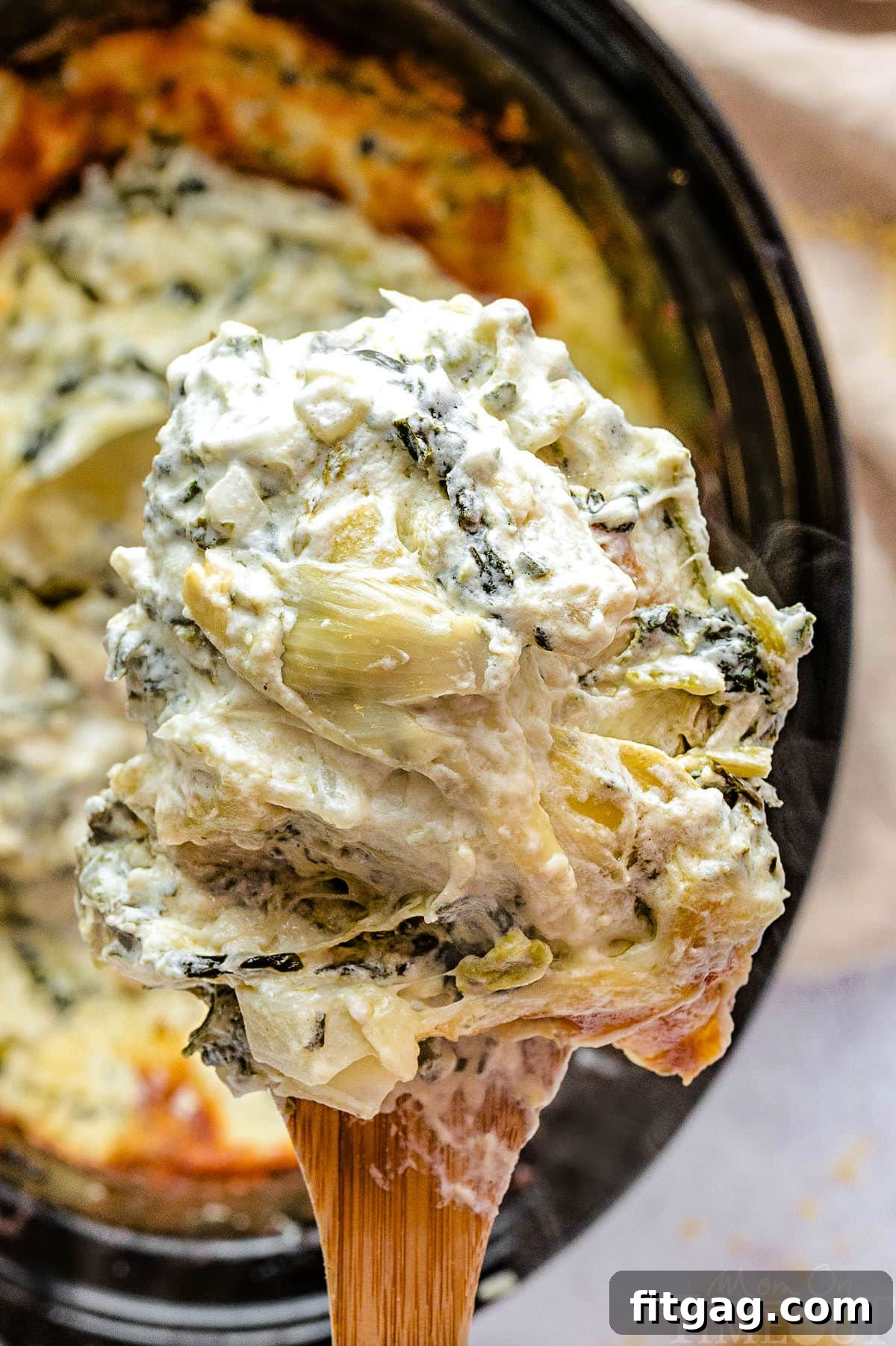 One Pot Wonder Spinach Artichoke Dip 3 Close-up of creamy Crockpot spinach and artichoke dip being scooped with a large wooden spoon from the slow cooker.