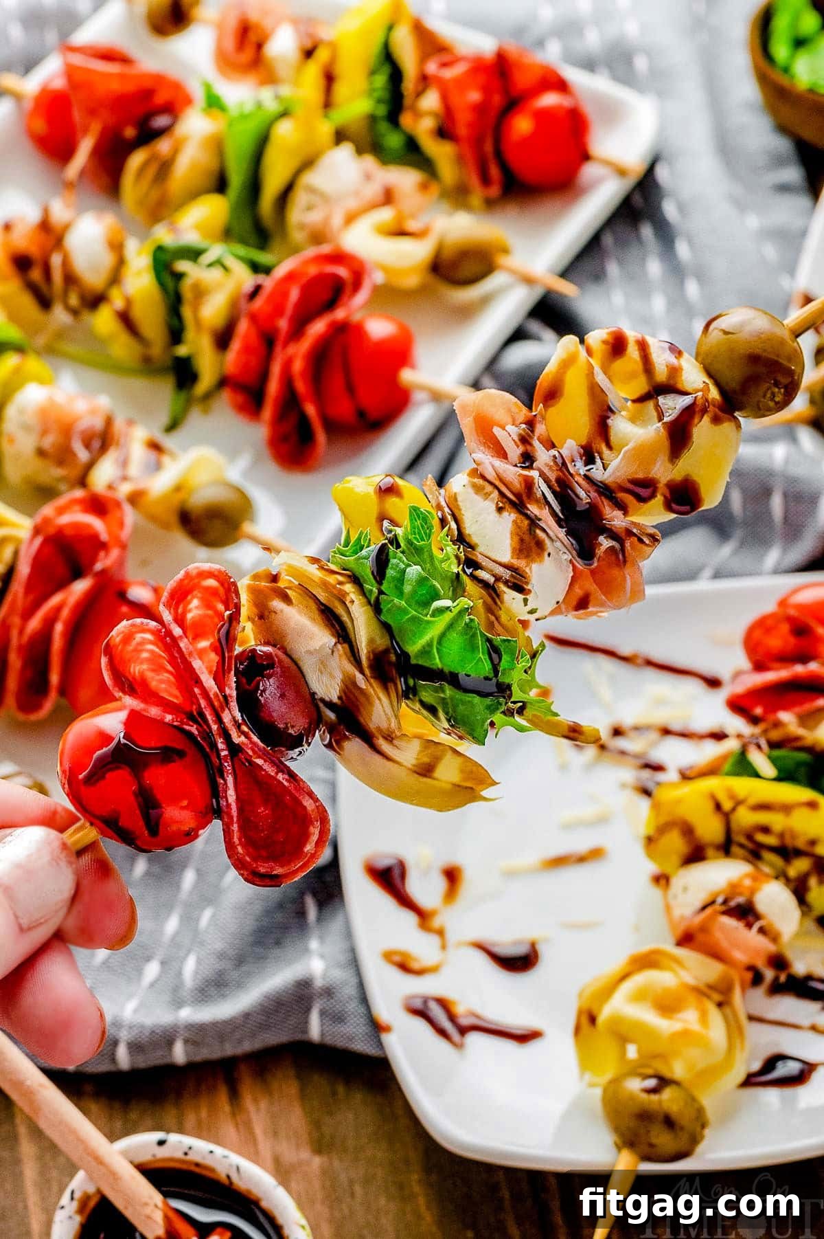 Hand holding up a single antipasto skewer over a serving plate, highlighting the layered ingredients.