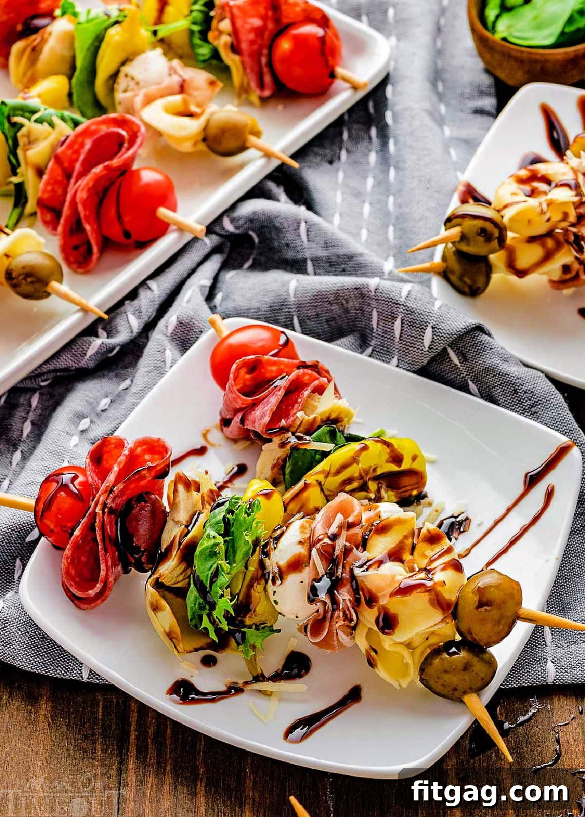 Two antipasto skewers artfully arranged on a white plate, garnished with a generous drizzle of balsamic glaze.
