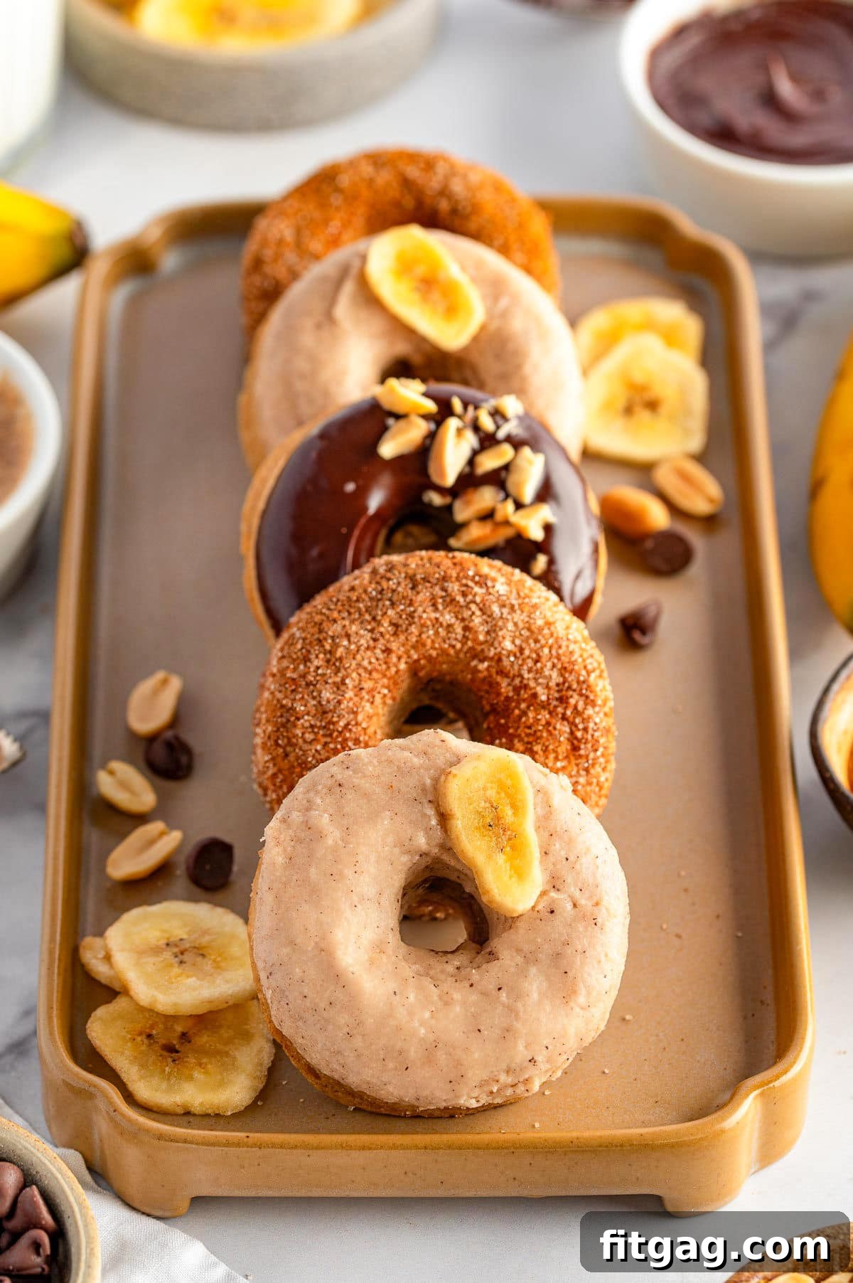 Banana Bliss Donuts 9 Banana Donuts leaning against each other on a pretty decorative tray. Toppings are on the tray next to the donuts.
