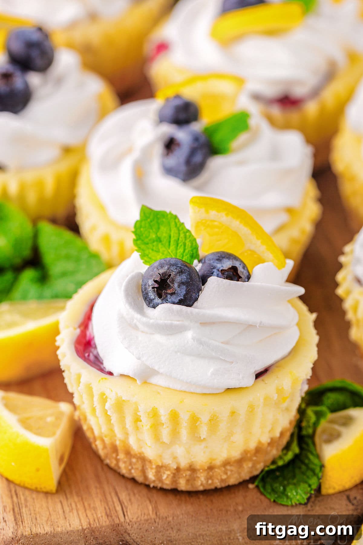 A close up view of a lemon blueberry mini cheesecake. Garnishes and more cheesecakes are behind it.