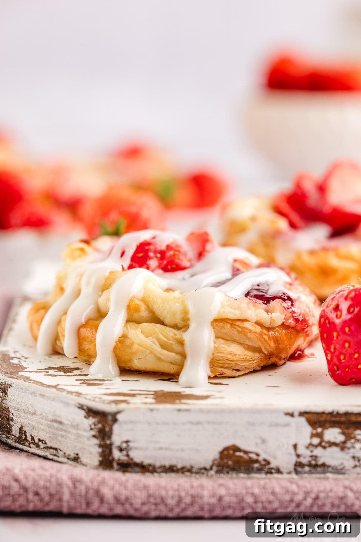Strawberry Danish Delight 6 A freshly baked Strawberry Cream Cheese Danish, beautifully drizzled with glaze, resting on a white wooden board, ready to be enjoyed.