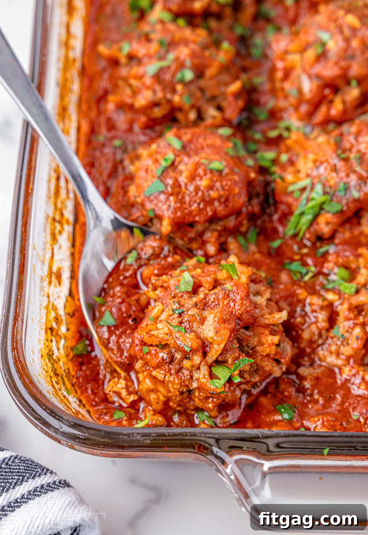 Rice Quilled Meatballs 3 Porcupine meatballs in a glass baking dish. A metal spoon is holding one of the meatballs.
