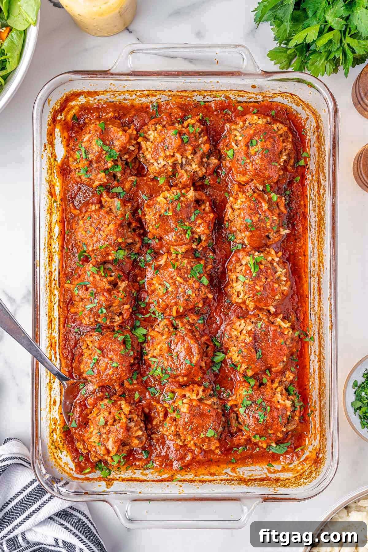 Rice Quilled Meatballs 4 Porcupine Meatballs with fresh parsley sprinkled on top. The meatballs are lined up in a baking pan. A metal spoon is holding one of the meatballs.