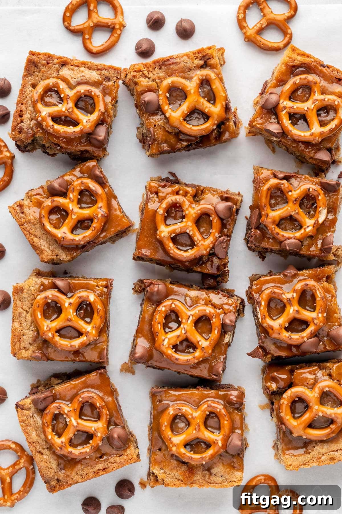 Salted Caramel Pretzel Blondies lined up on a piece of parchment paper. Pretzels and chocolate chips are scattered around the bars.