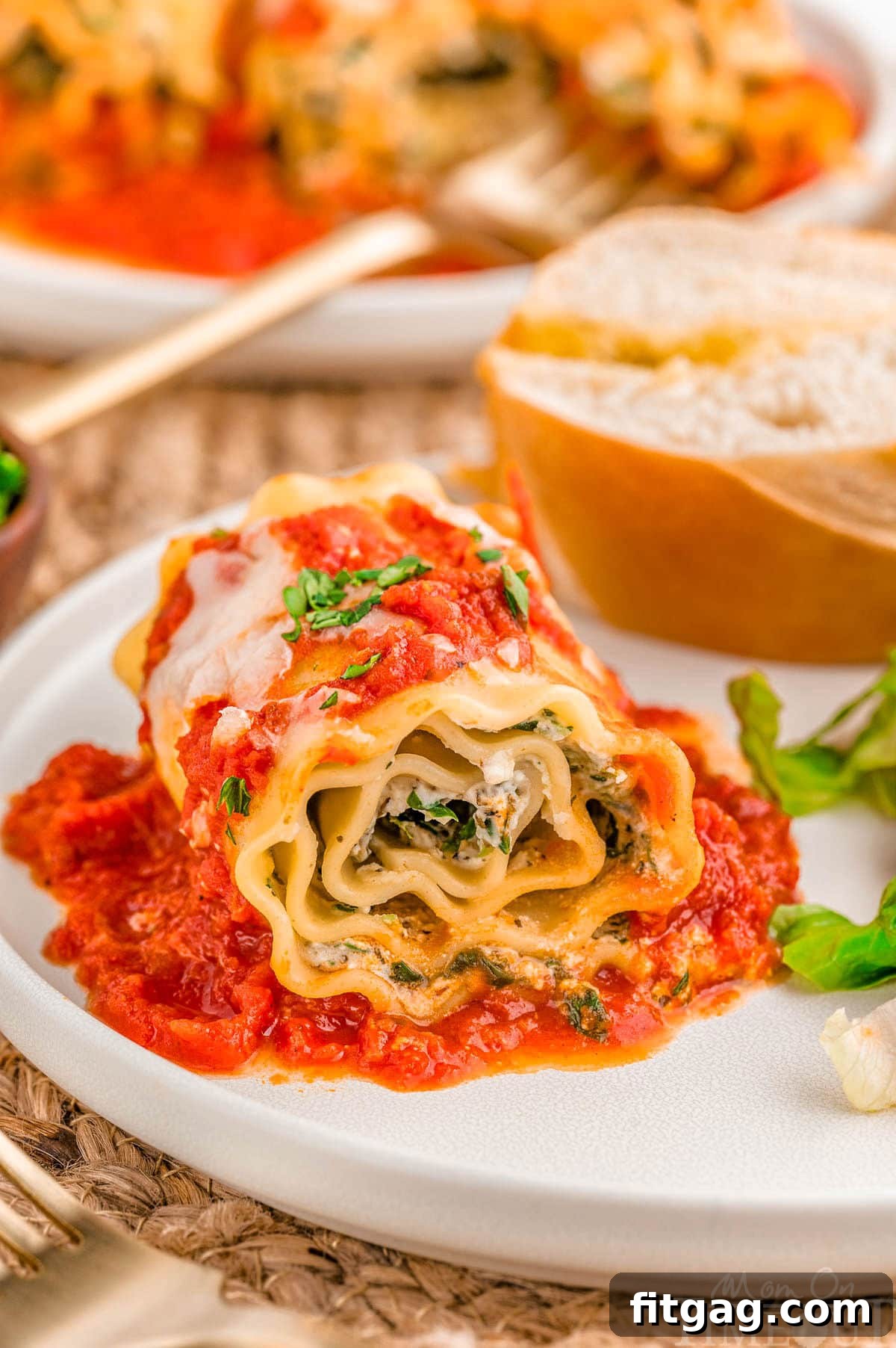 Lasagna Pinwheels 2 Lasagna Roll Ups plated with salad and bread on a dinner plate.