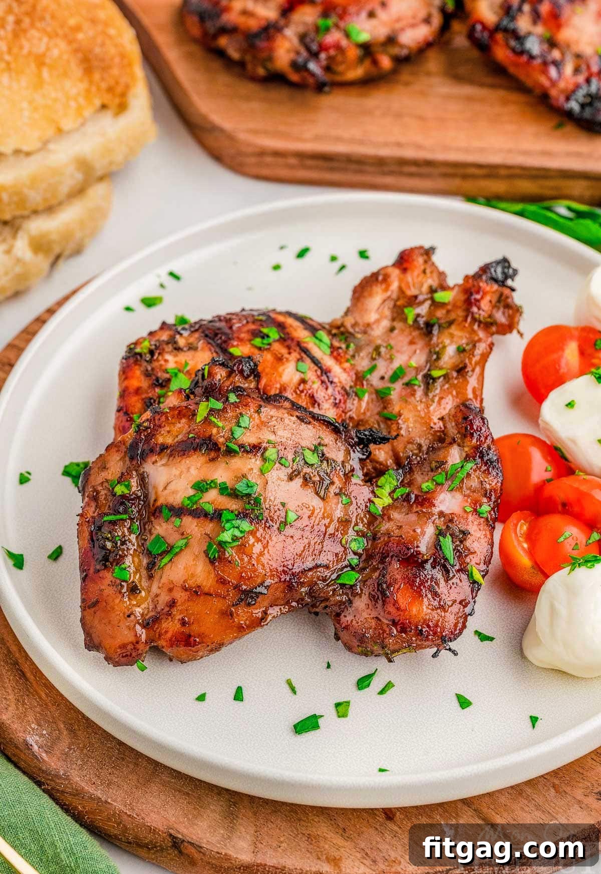 Two pieces of grilled balsamic chicken on round white plate with mozzarella and tomatoes.