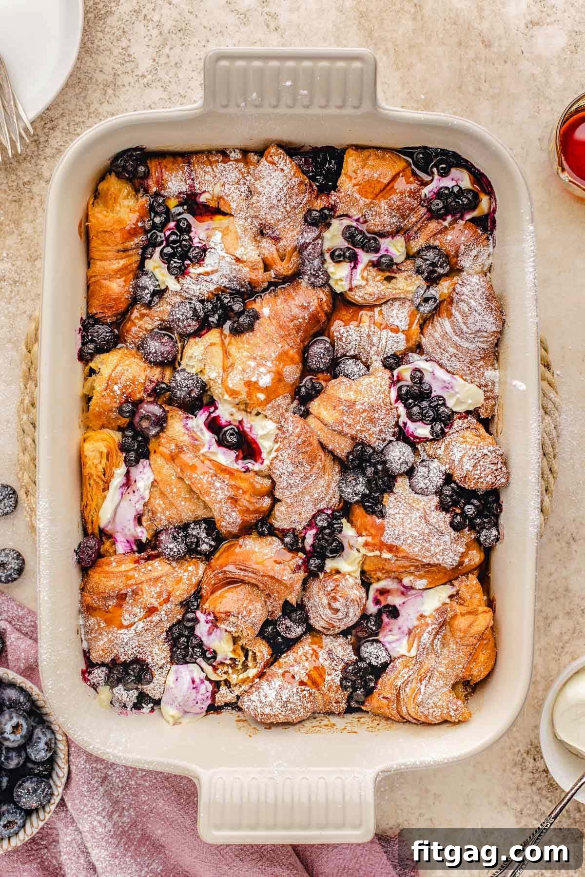 Top down look at croissant french toast bake in baking dish made with blueberries and topped with a dusting of powdered sugar. A perfect make-ahead brunch or holiday breakfast.