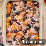 Top down look at croissant french toast bake in baking dish made with blueberries and topped with a dusting of powdered sugar.