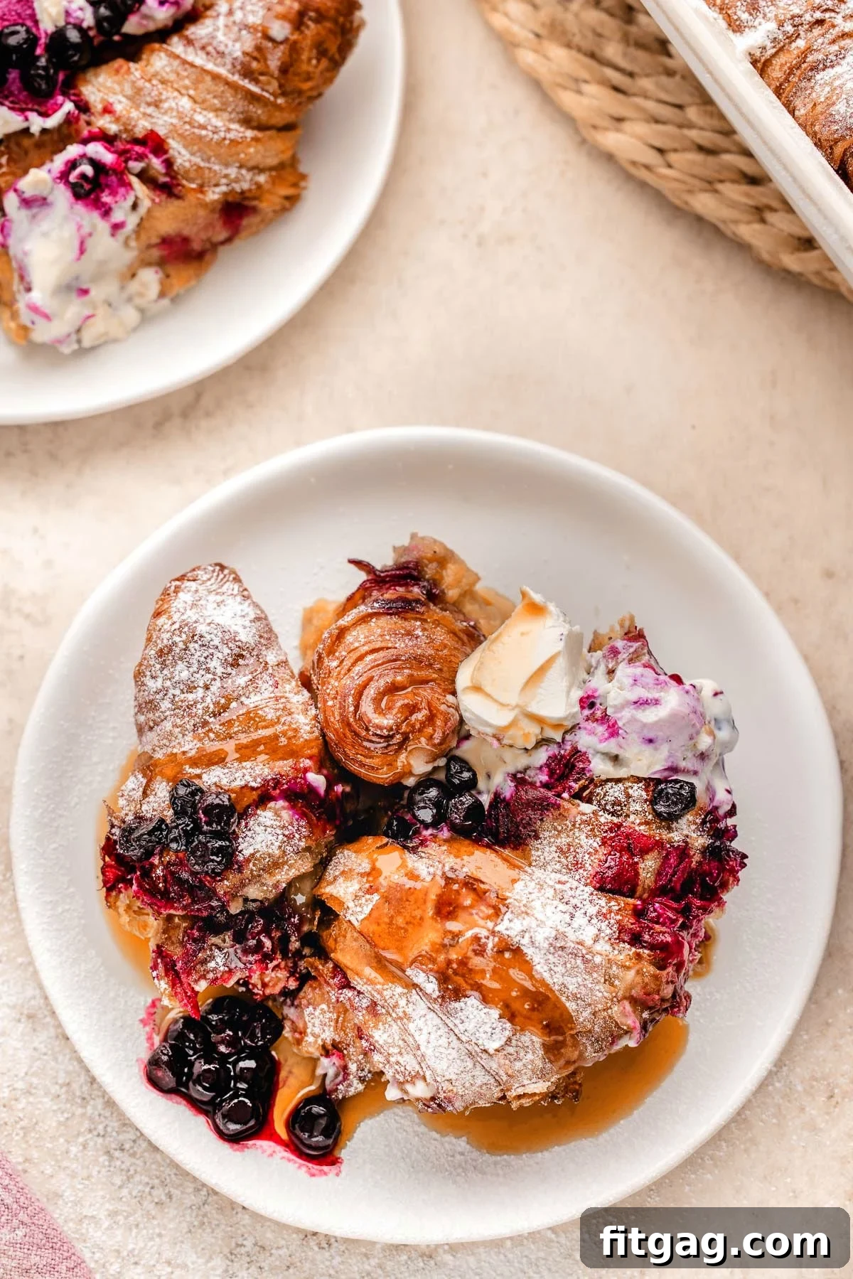 Close-up view of a slice of Blueberry Croissant French Toast Bake on a white plate, garnished with maple syrup and fresh blueberries.