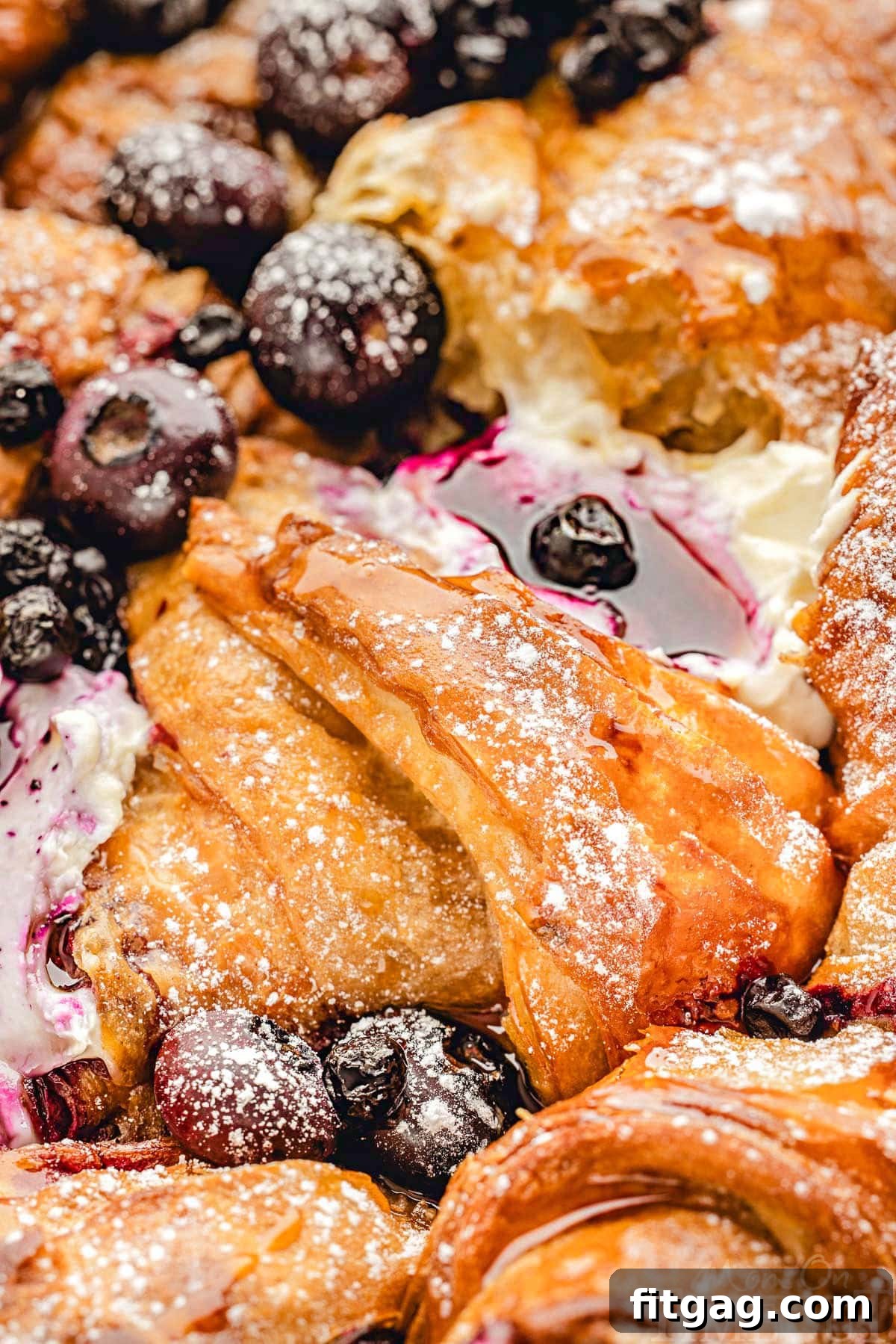 Close-up of golden-brown Blueberry Croissant French Toast Bake glistening with maple syrup and scattered blueberries.