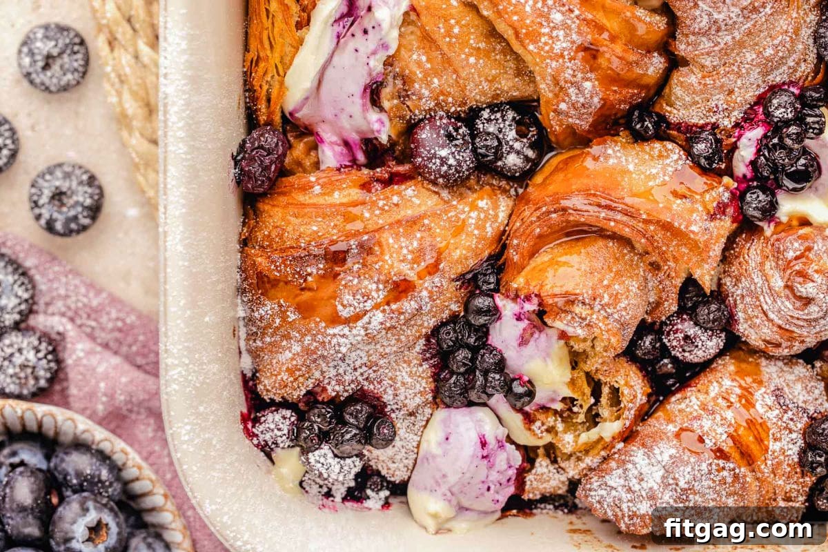 Wide angle view of a freshly baked blueberry croissant French toast bake in a baking dish, with visible blueberries on the side.