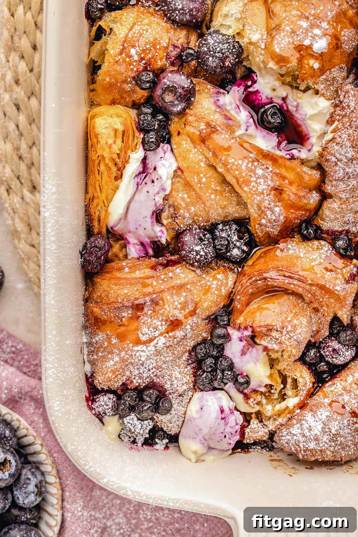 Overhead shot of a baked blueberry croissant breakfast bake in a dish, dusted with powdered sugar, ready to serve.