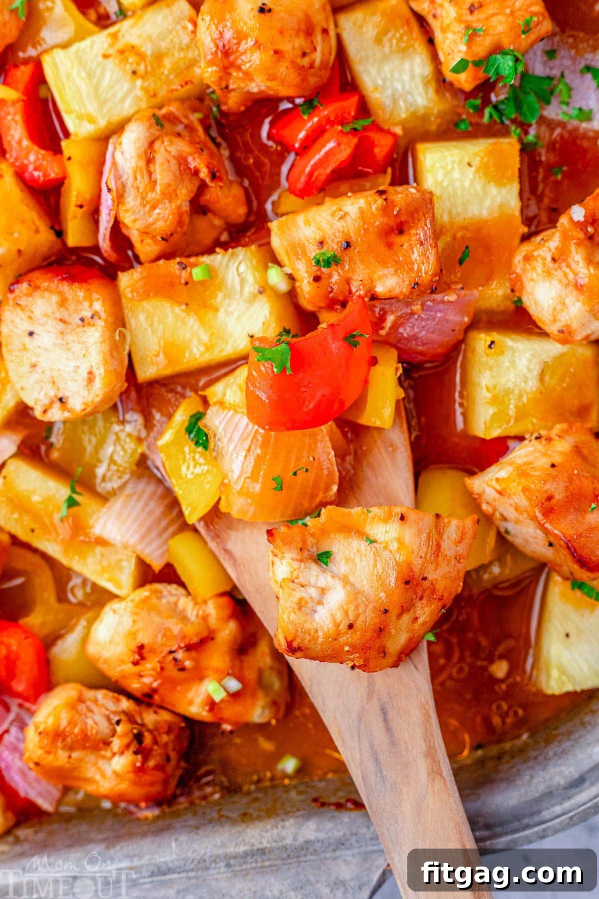 Hawaiian chicken on sheet pan with a wooden spoon scooping up the chicken and vegetables, highlighting the sticky glaze and charred edges.