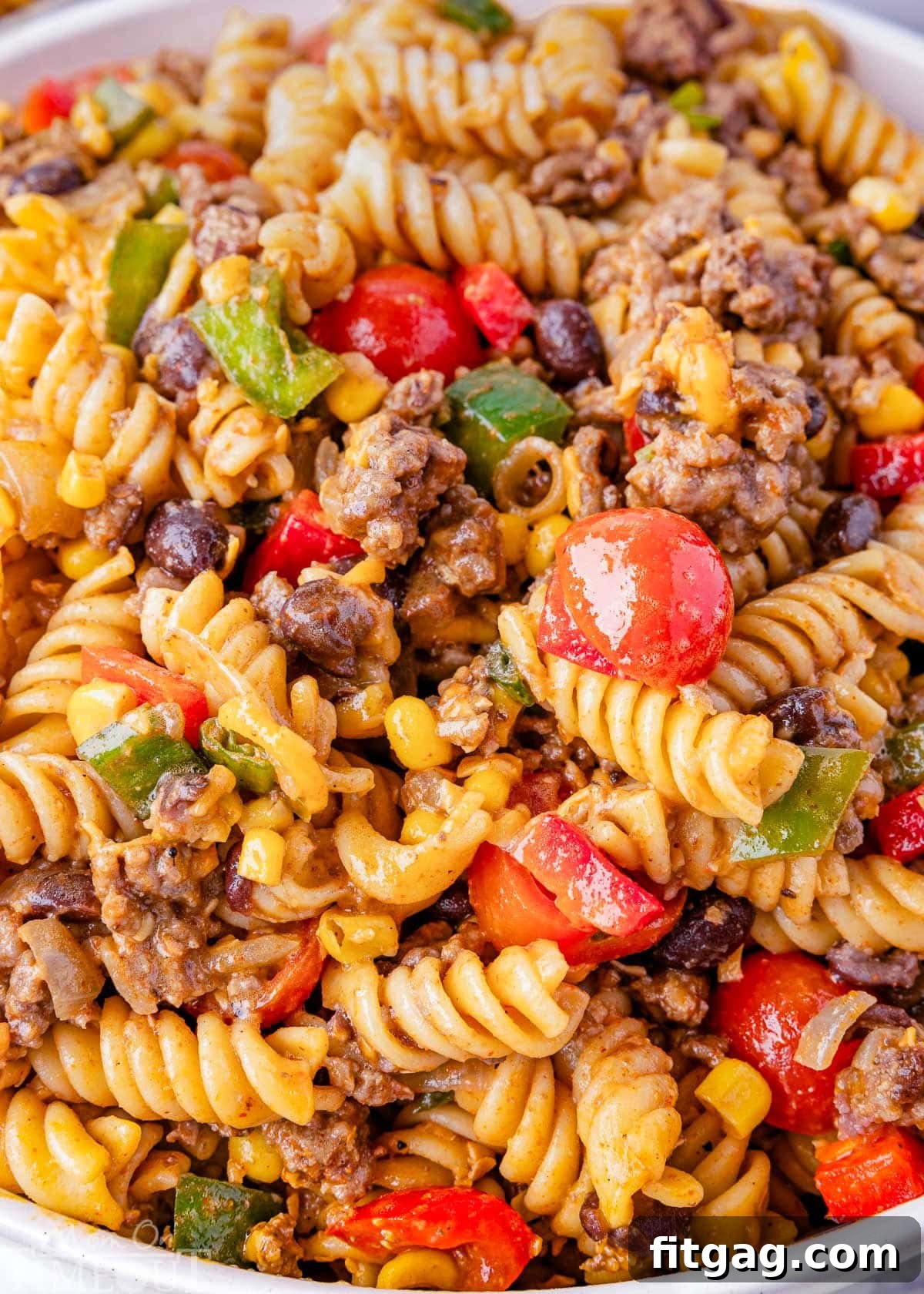 Chuckwagon Pasta Salad 5 A close-up shot of the Cowboy Pasta Salad, highlighting individual components like vibrant cherry tomatoes, seasoned ground beef, spiral pasta, crisp bell peppers, cubes of cheddar cheese, and sliced green onions, all beautifully tossed in a zesty lime and taco dressing.