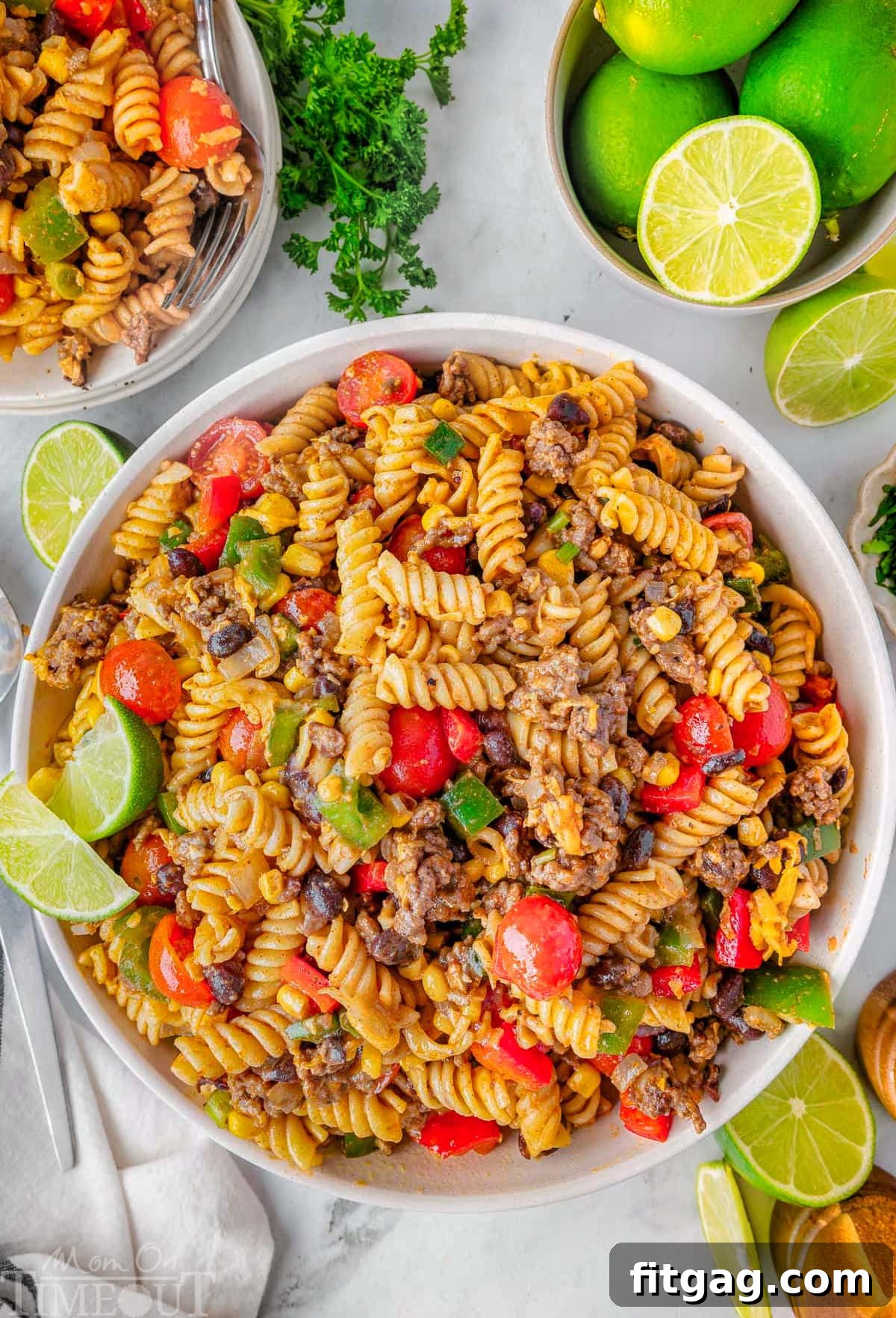 Chuckwagon Pasta Salad 7 An overhead view of the finished Cowboy Pasta Salad recipe presented in a large, pristine white bowl, elegantly garnished with fresh lime wedges for a zesty touch.