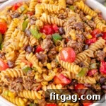 Big serving bowl of Cowboy Pasta Salad ready to be served. A plate of the salad can be seen in the background along with a few limes.