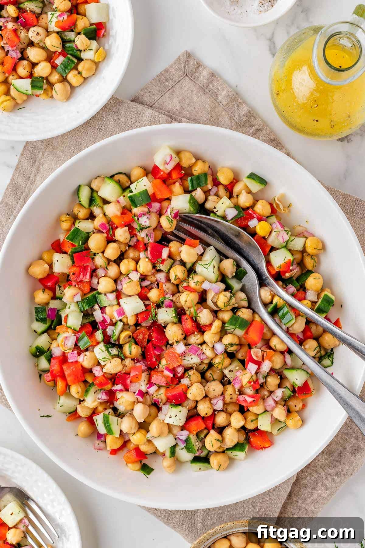 Overhead view of a white bowl filled with fresh chickpea salad, featuring diced cucumbers and a light vinaigrette.