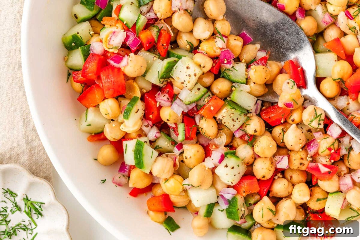 Wide shot of garbanzo bean salad in white bowl with serving spoon.