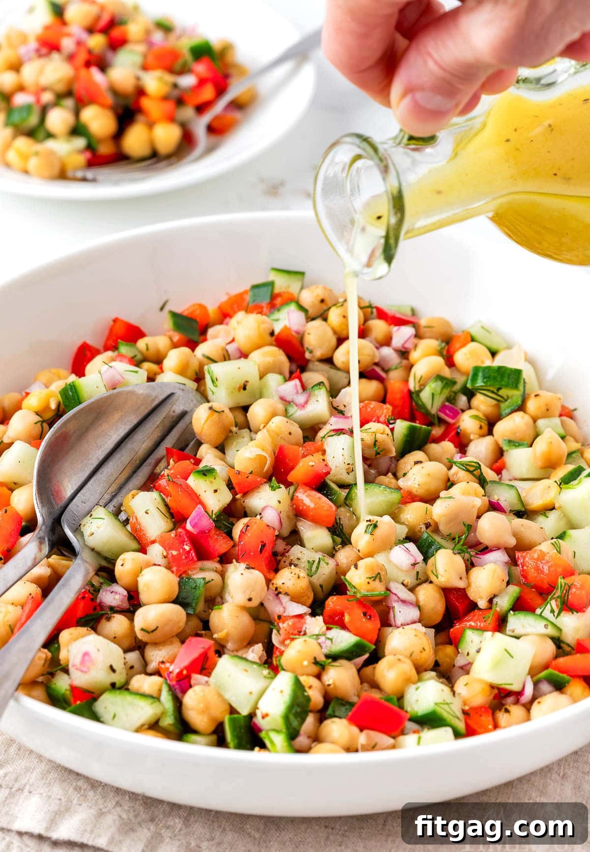 Close-up of a tangy dressing being generously poured over fresh chickpea salad in a pristine white bowl.