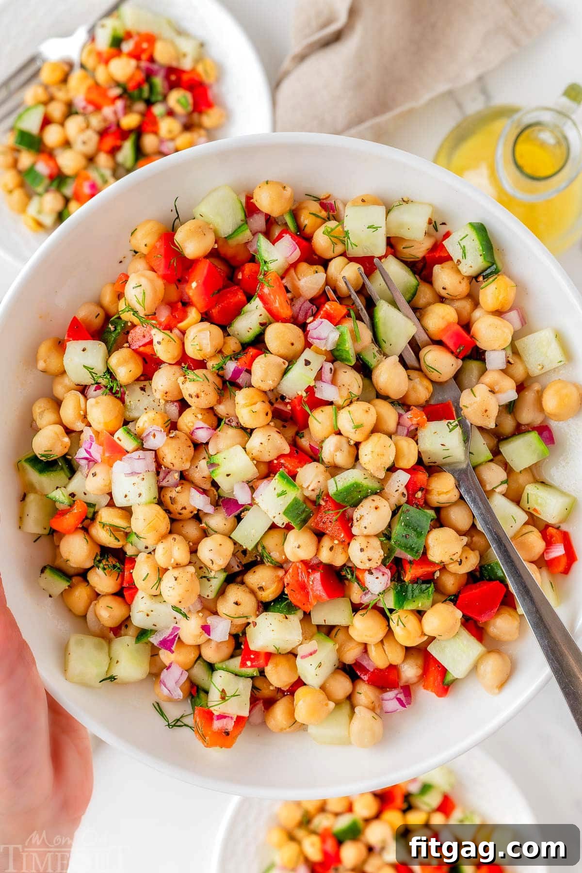 Bowl of chickpea salad recipe being held up over two small plates with the salad on them.