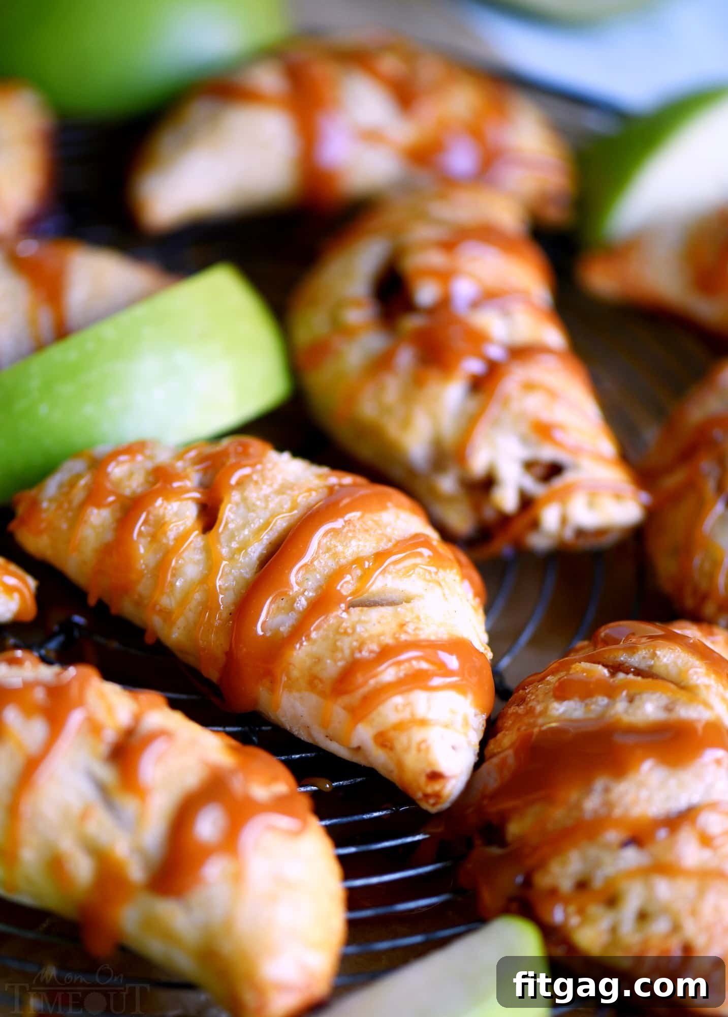 Freshly baked caramel apple empanadas on a baking sheet, drizzled with caramel.