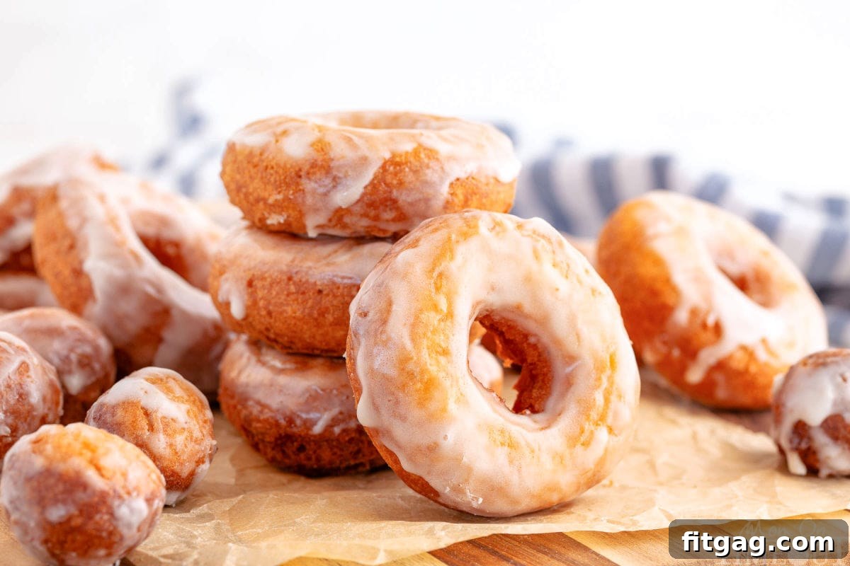 Wide shot of full batch of sour cream cake donuts on brown parchment glazed and ready to eat.