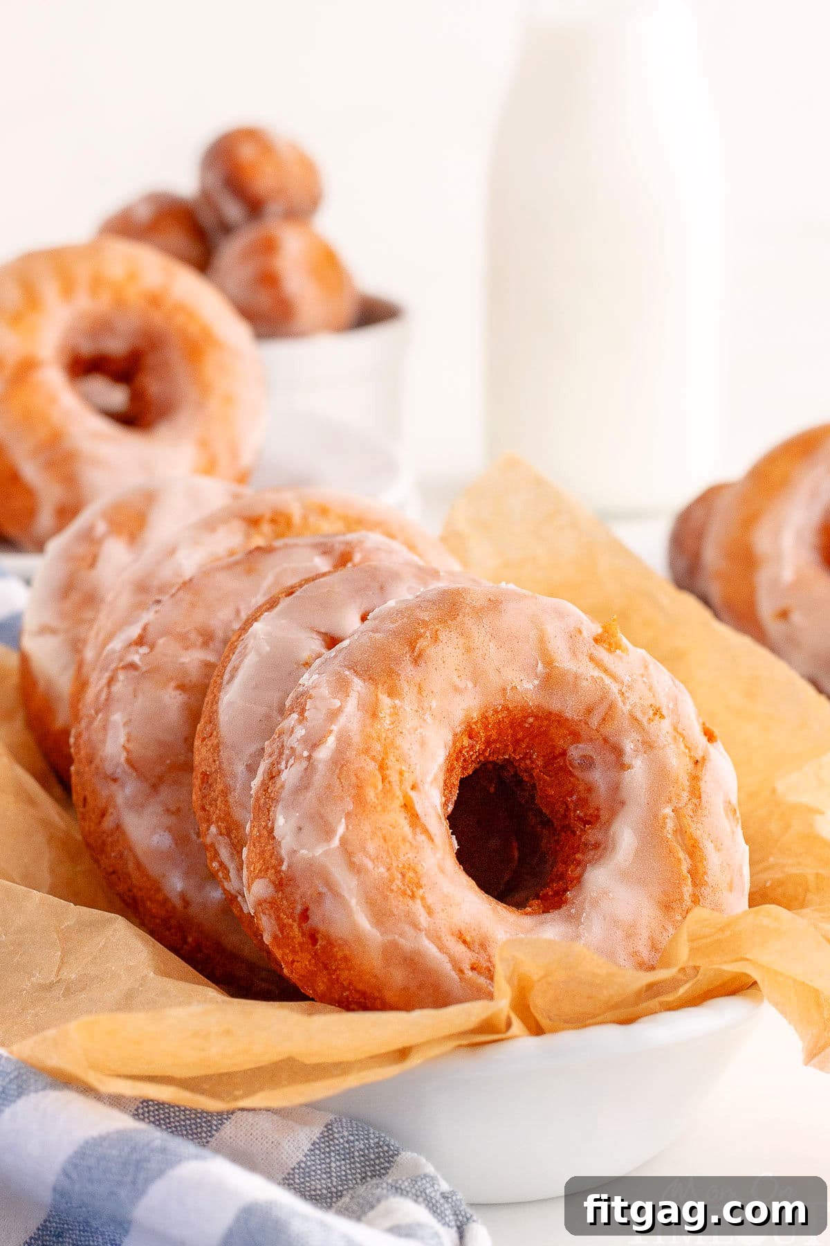 Sour Cream Cake Donuts in white dish lined with parchment. More donuts can be seen in the background.