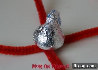 All four pipe cleaner ends pulled up and twisted tightly around the tip of the Hershey's Kiss to secure it.