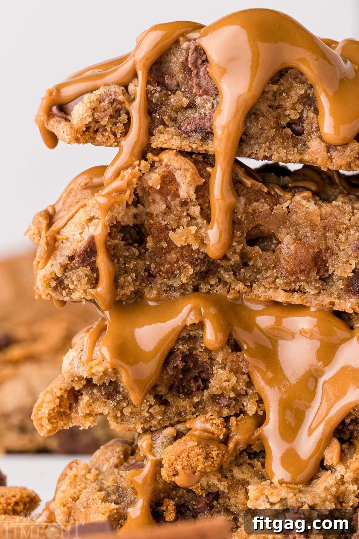 Golden Speculoos Chocolate Chip Dreams 6 A close-up view of chocolate chip Biscoff cookies, with one torn in half to reveal its soft interior and melty chocolate. Four cookies are stacked high, with a tempting drizzle of cookie butter on top. More cookies are visible in the background.